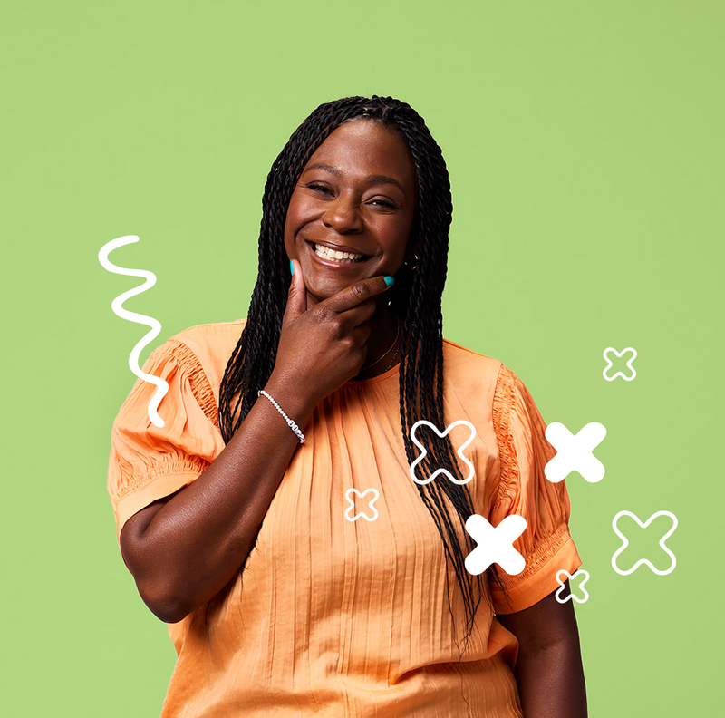 A smiling woman wearing an orange shirt with her hand on her chin.