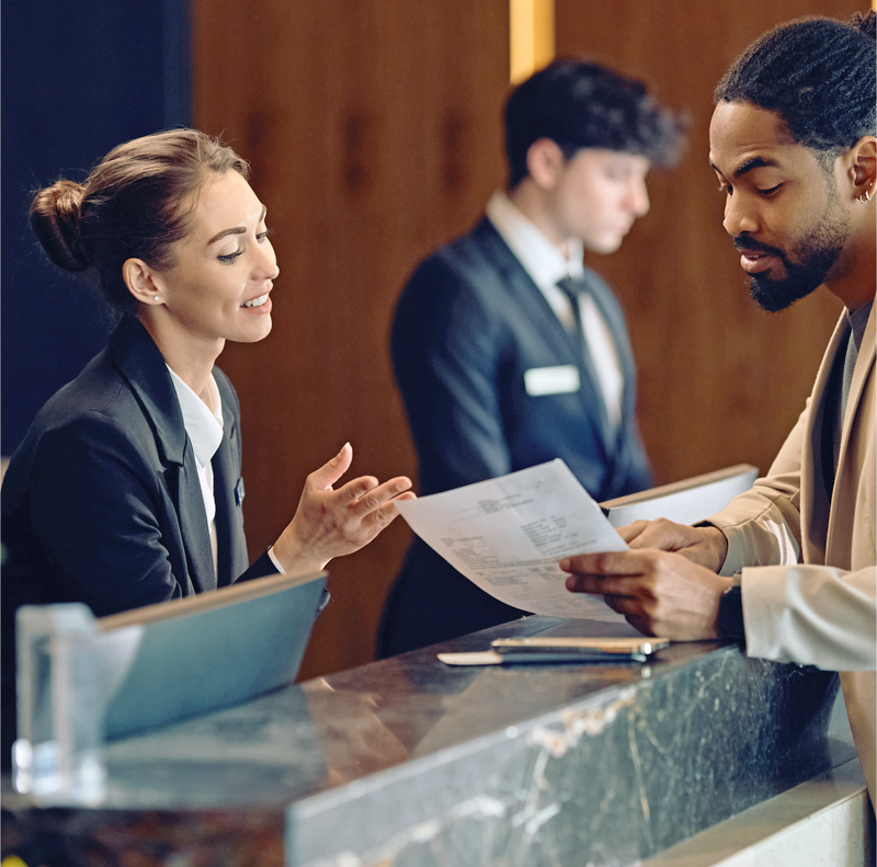 Two people at the front desk of a hotel reviewing a print out.