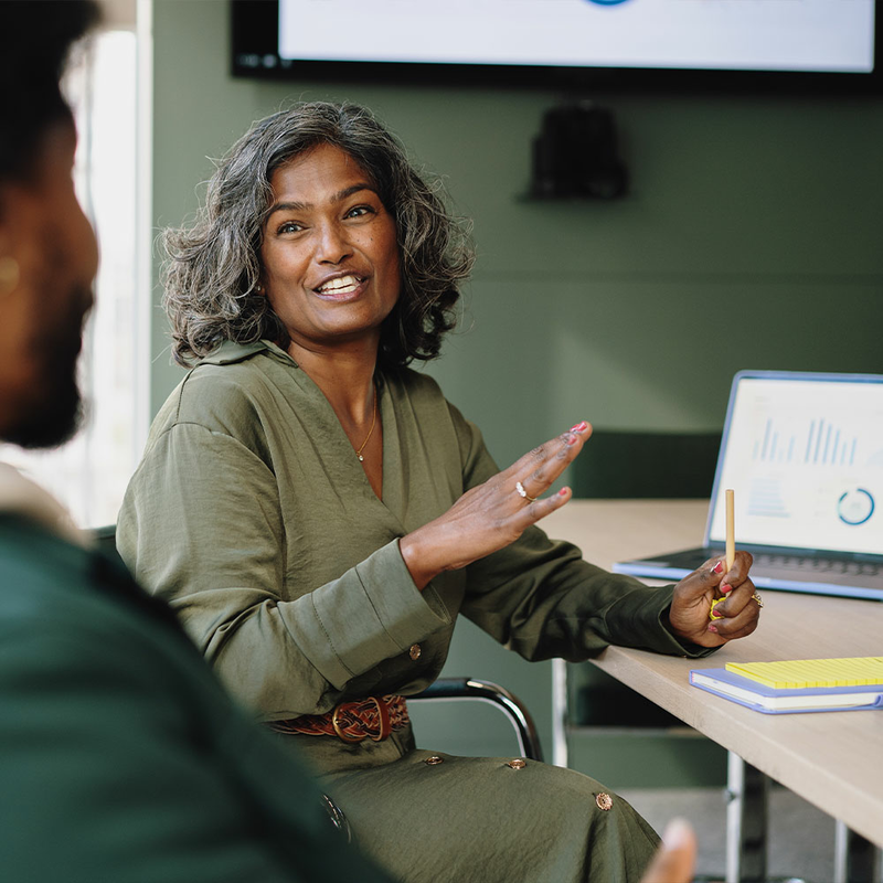 Manager sitting at a conference table in an office smiling and talking to a man sitting beside her