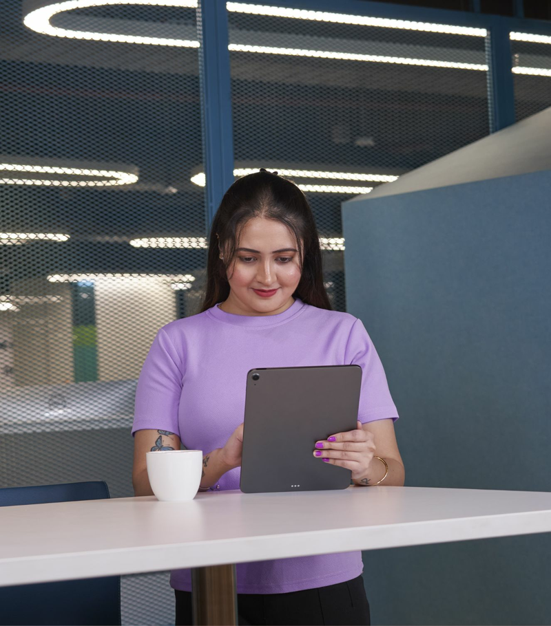 A woman in a purple shirt is standing in an office, looking at a tablet.