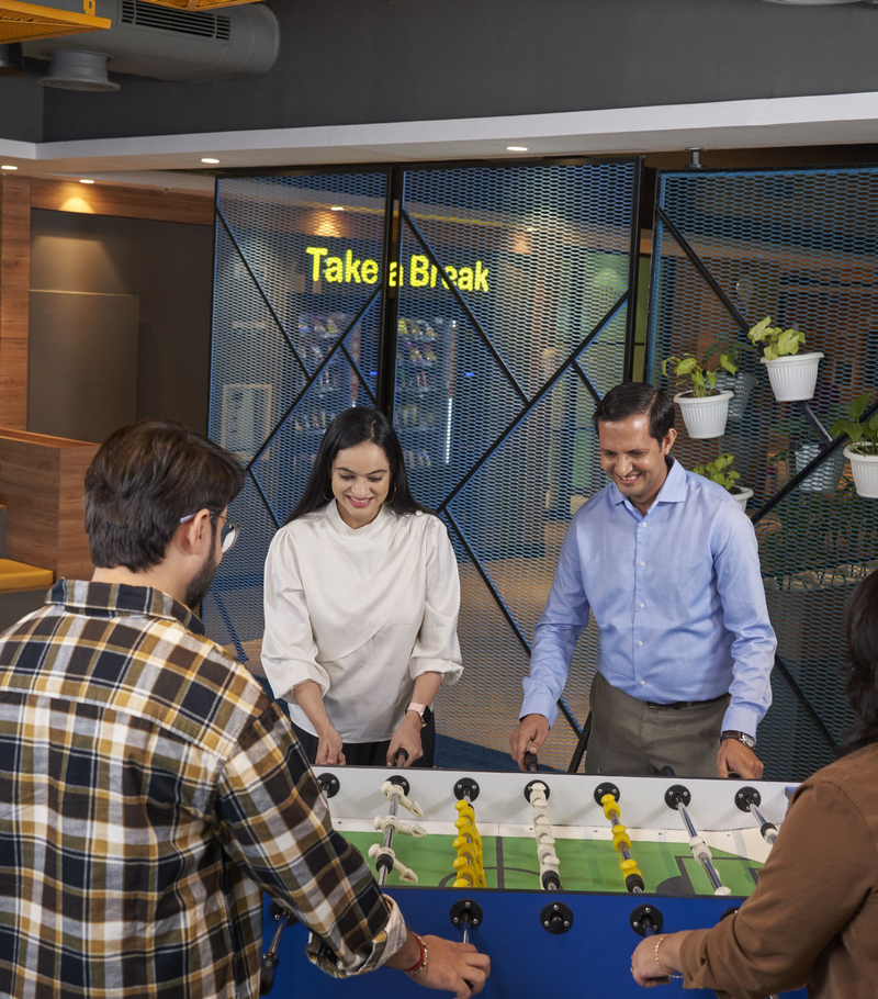 A group of four coworkers are playing foosball in the break room.