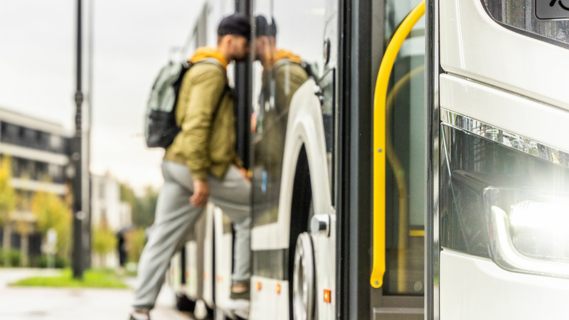 A young man with a backpack is getting on a bus.