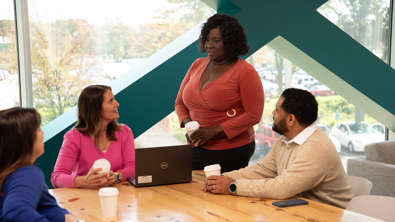 A group of women at work sitting around a table listening to a women standing next to them