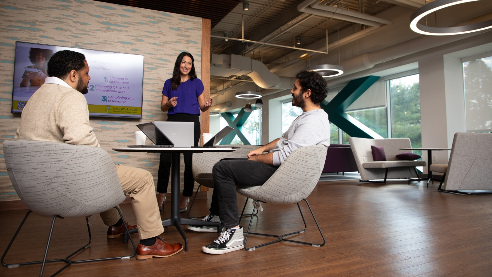 A woman stands in front of two men who are sitting at a table.