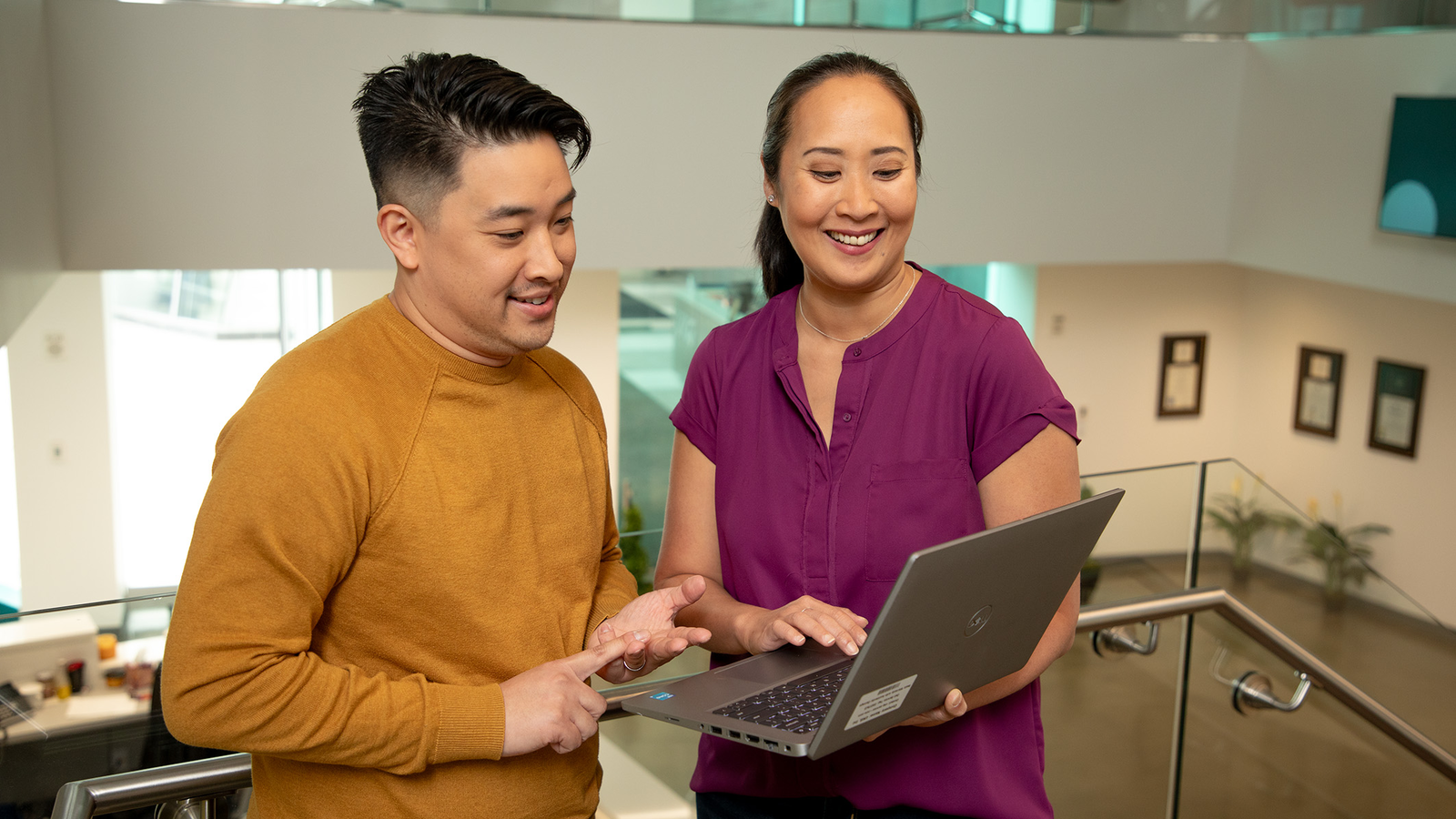  A man and a woman are standing in a brightly lit room looking at a laptop.