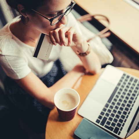 A women looking at her laptop with a credit card in her hand and coffee on the table