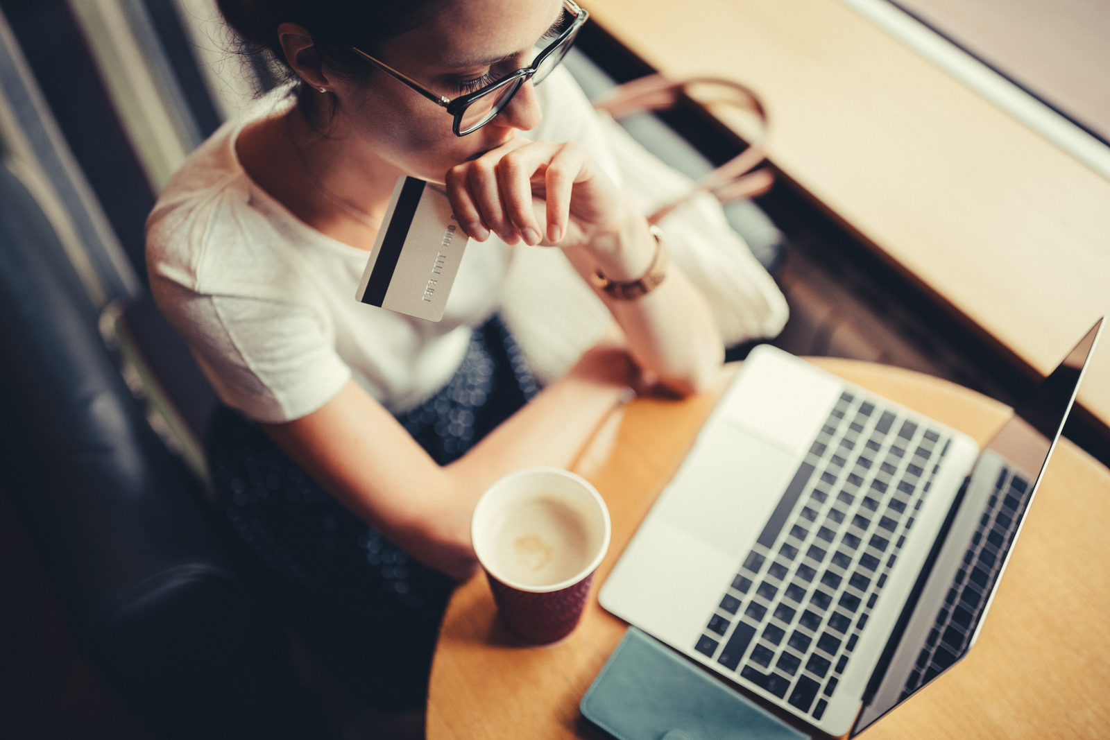 A women looking at her laptop with a credit card in her hand and coffee on the table