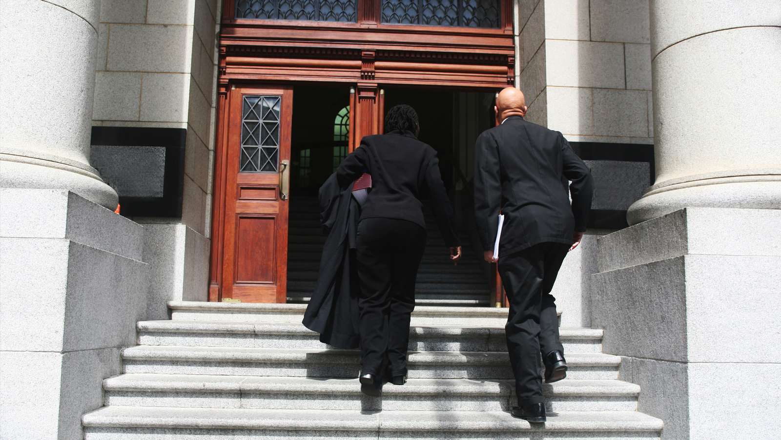 Two people in business suits walk up the stairs of a government building.