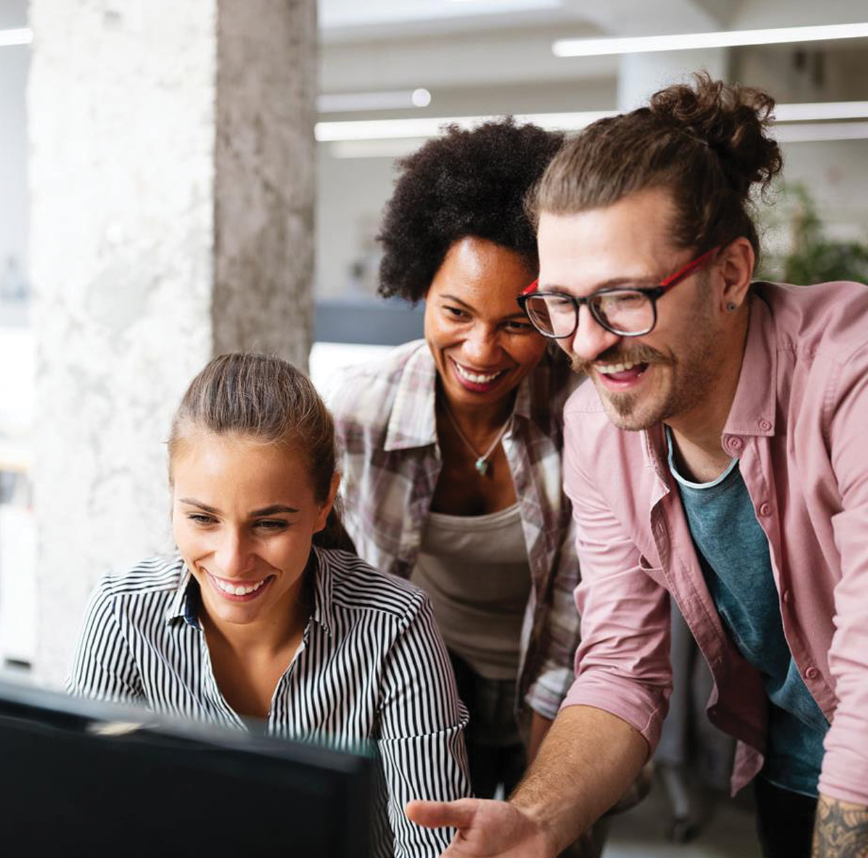  Three smiling business people looking at a computer monitor.