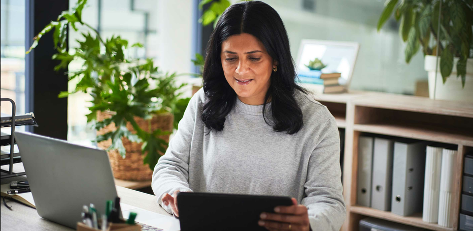 Woman sitting at her desk in a home office looking at her tablet device smiling