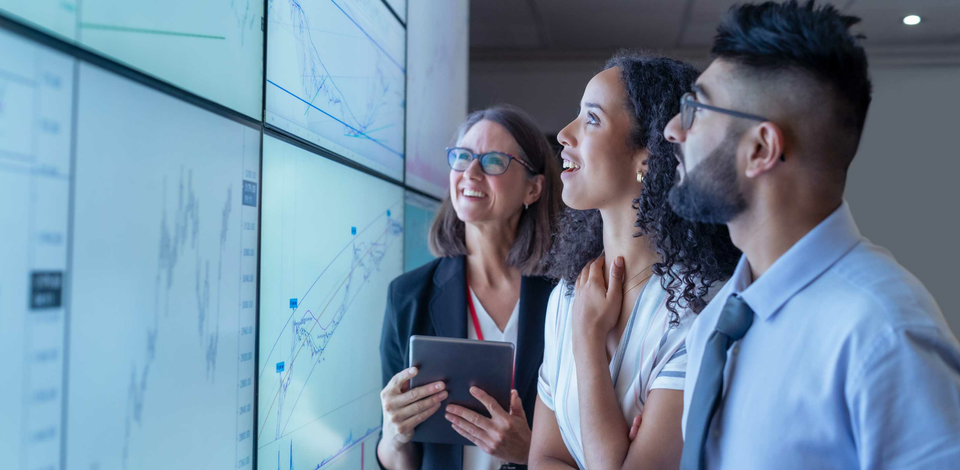 Office setting where 3 employees are smiling at a large screen of data 