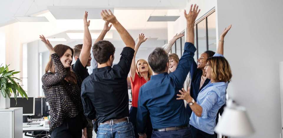 A group of happy employees in an office raising their hands and giving high fives