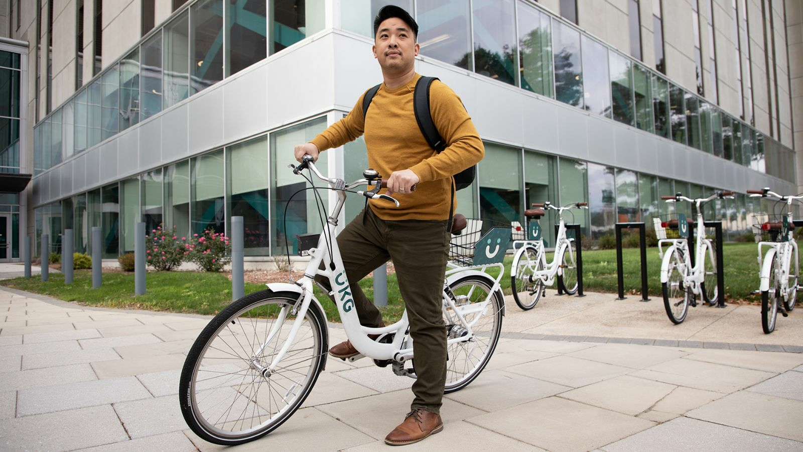 A man in a yellow sweater and khaki pants stands next to a white bicycle.