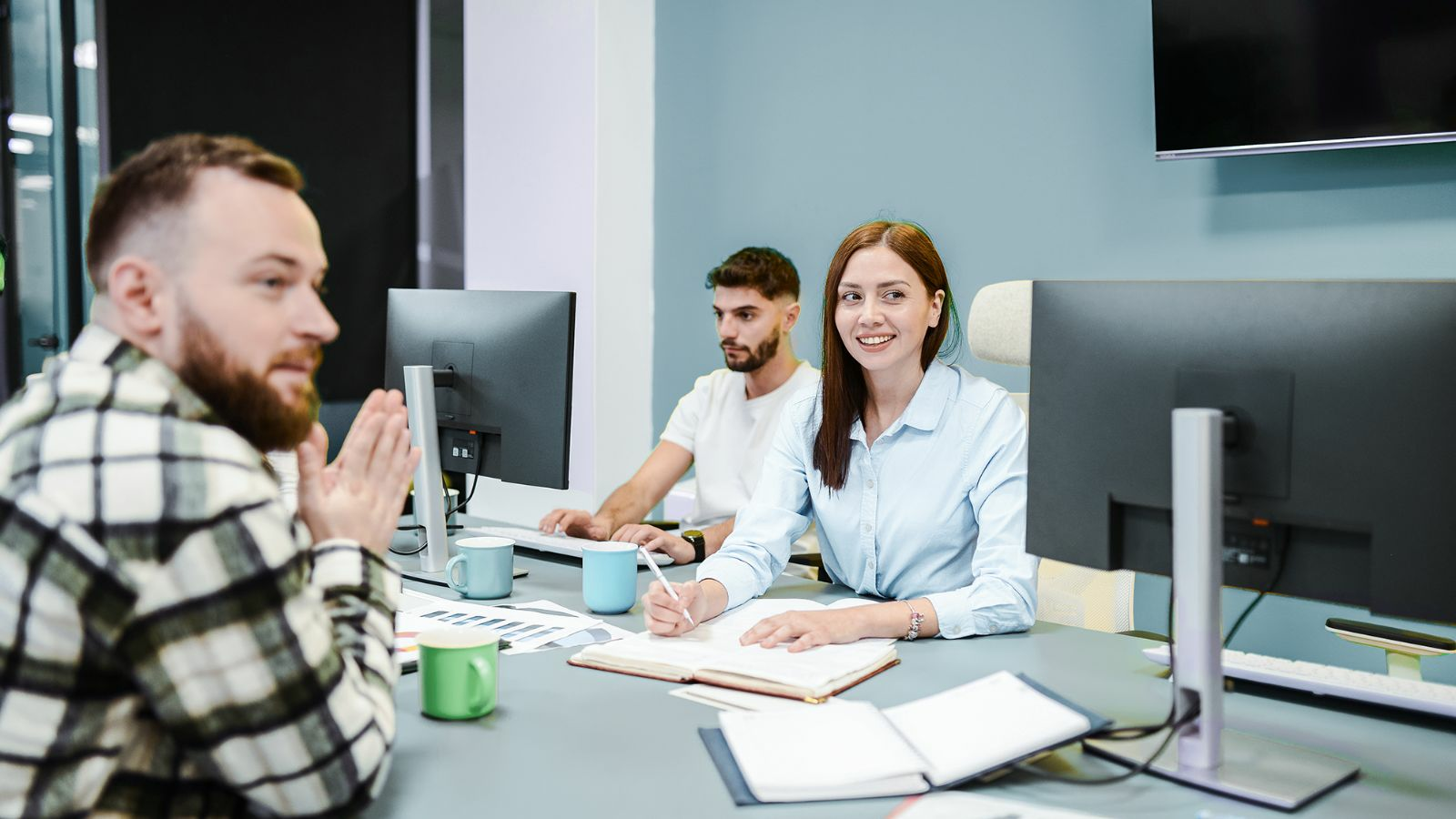 A woman sits at a conference table in a meeting writing in a notebook.