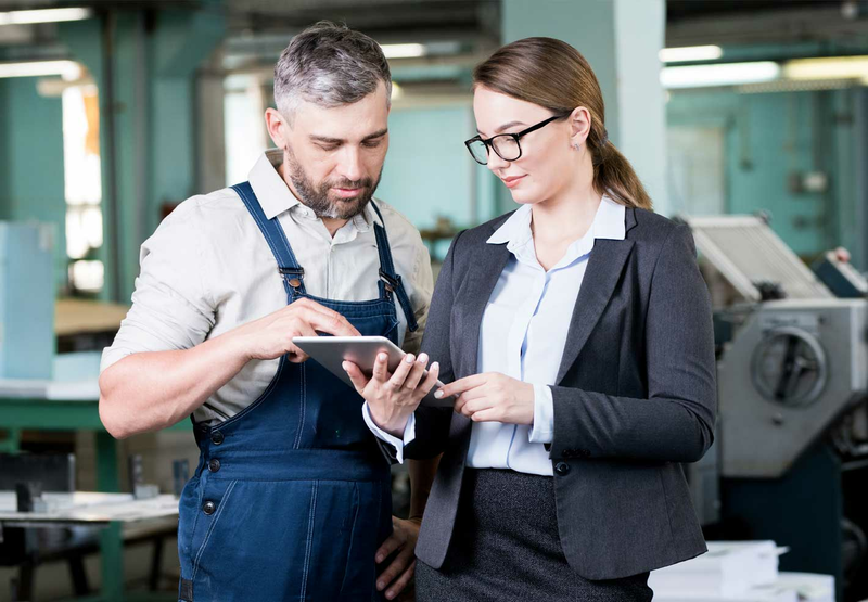 A man and woman in a factory are looking at a tablet together.