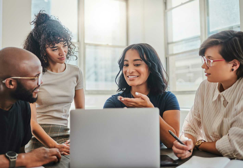 A group of four business professionals are having a meeting in an office and looking at a laptop.