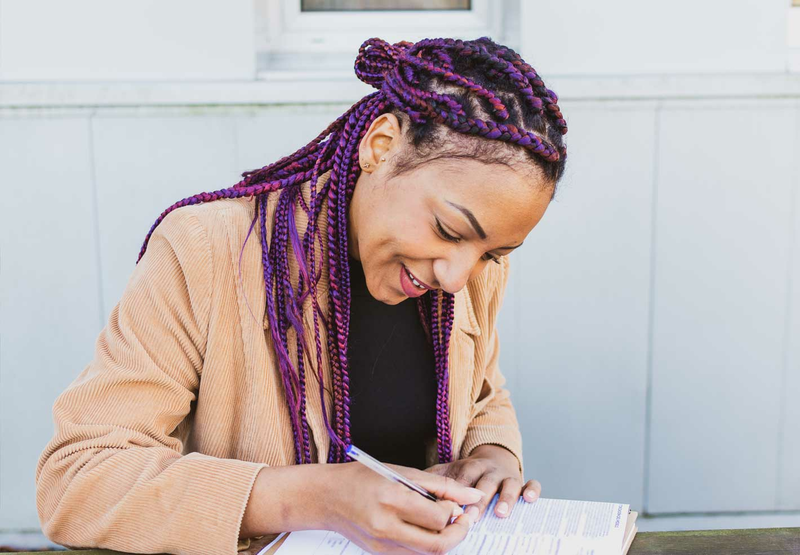 A young woman with purple braids is writing on a clipboard.