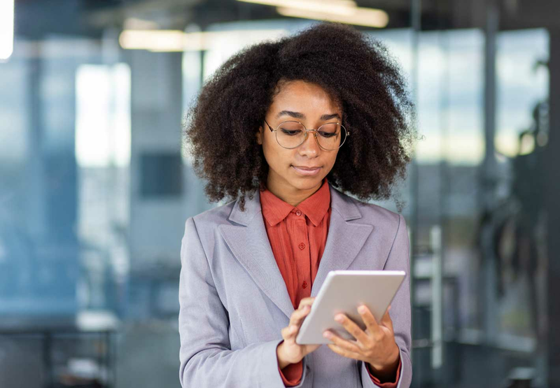 A young woman in a suit and glasses is looking down at a tablet.