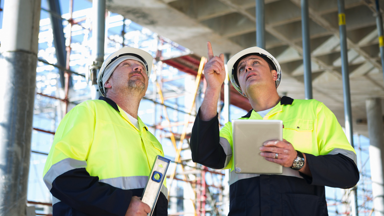  Two construction workers in hard hats and safety vests are looking up at a building