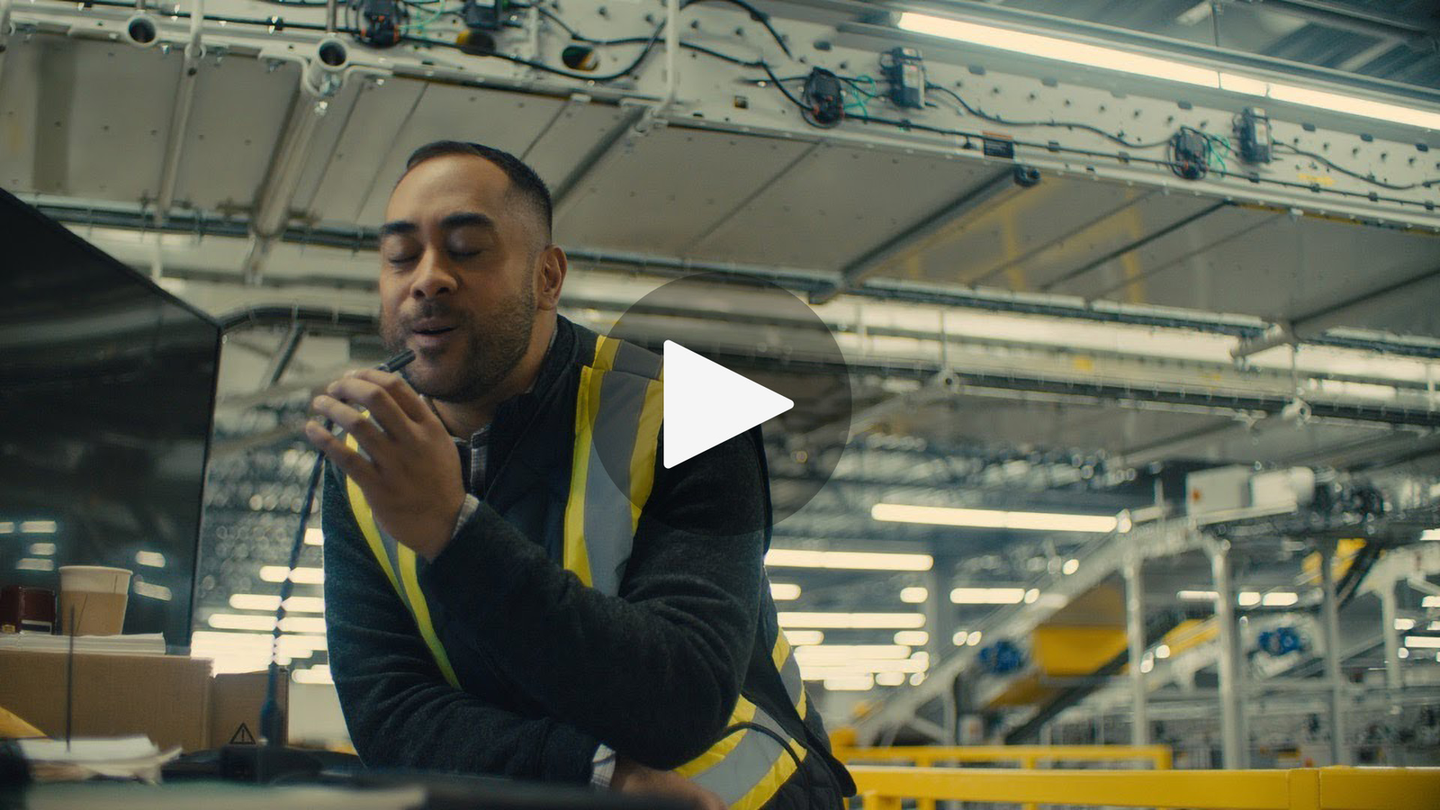  A man wearing a yellow vest is talking into a headset while working in a warehouse.