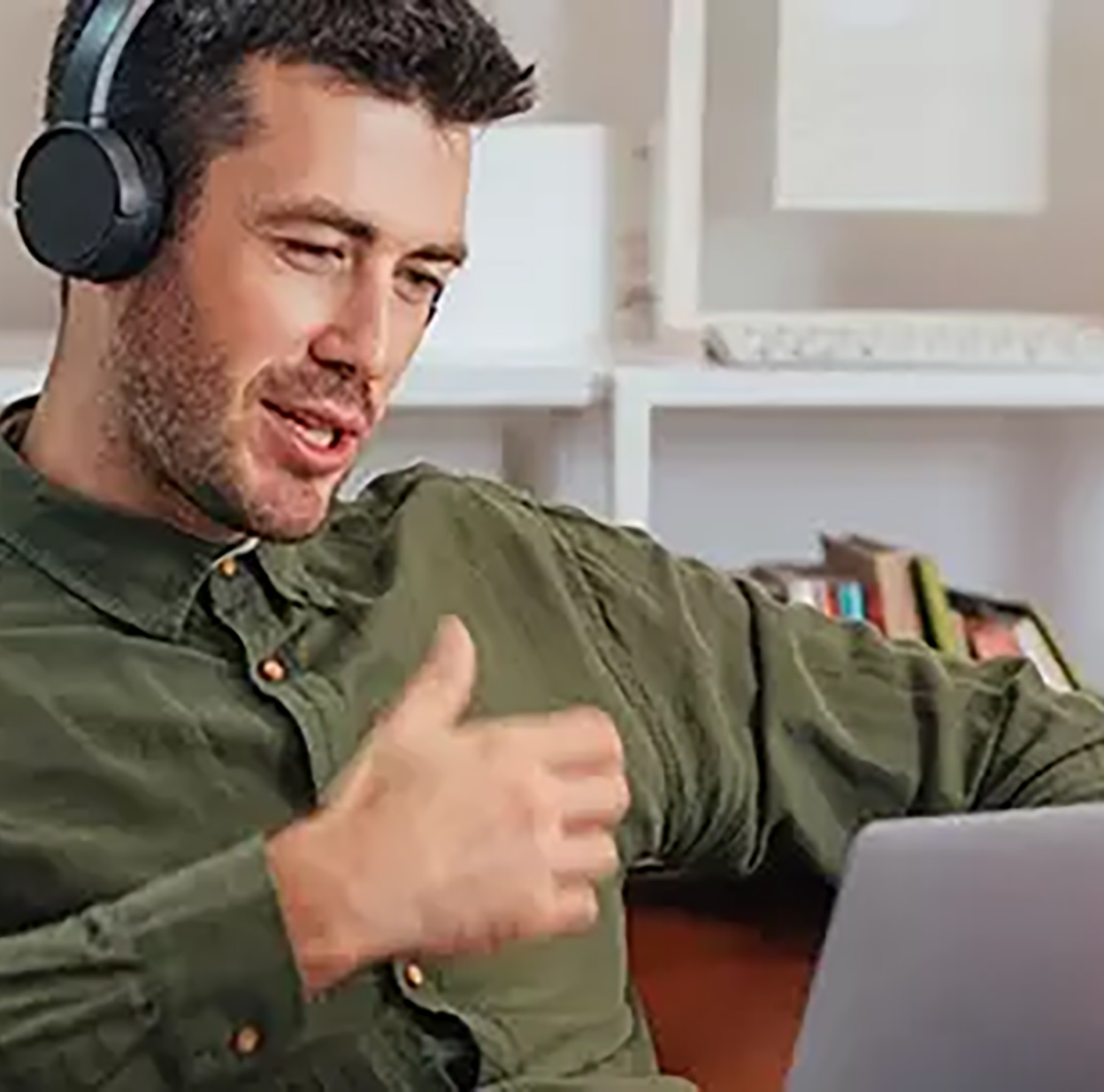  A man wearing headphones is sitting on a couch and talking to someone on his laptop.