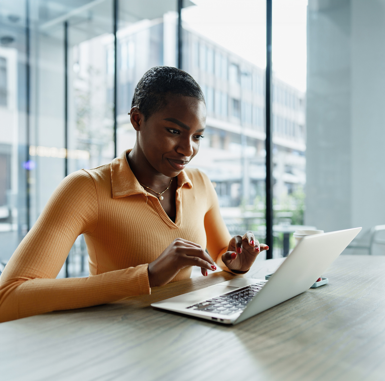  A person sits at a table and smiles while using a laptop.