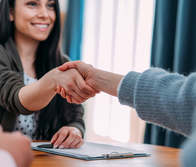 a woman shakes the hand of another person over a desk